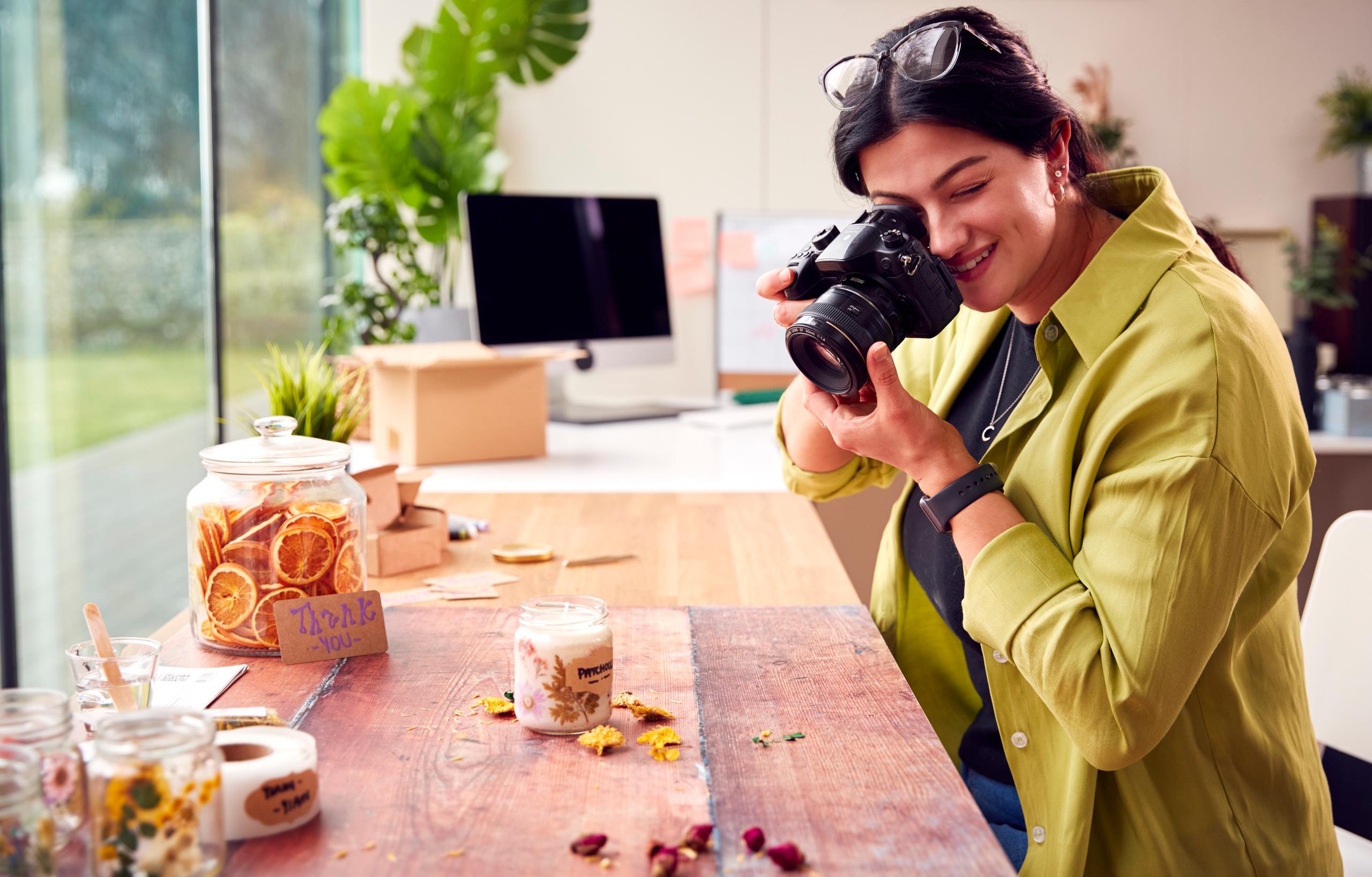 Colaborador de jShop tomando fotografías de producto para una tienda online. Artículos hechos a mano como velas y tarros de frutas secas sobre una mesa.